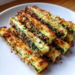 Close-up of crispy Air Fryer Zucchini Fries with Parmesan coating stacked on a white plate.