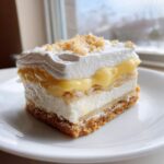 A layered slice of Banana Pudding Cheesecake Bars featuring a graham cracker crust, cheesecake layer, pudding, and whipped topping.