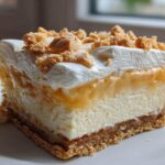 A layered square slice of Banana Pudding Cheesecake Bars featuring a crust, cheesecake, banana layer, whipped cream, and crumbled topping.