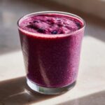Close-up of a thick, vibrant purple Blueberry Lemon Chia Smoothie in a clear glass, topped with whole blueberries.