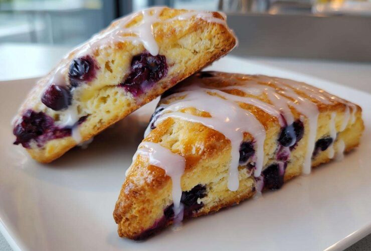 Close-up of two freshly baked Blueberry Lemon Scones drizzled with white lemon glaze, served on a white plate.