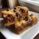 Close-up of two decadent Chewy Chocolate Chip Cookie Bars stacked on a white plate, featuring gooey melted chocolate.