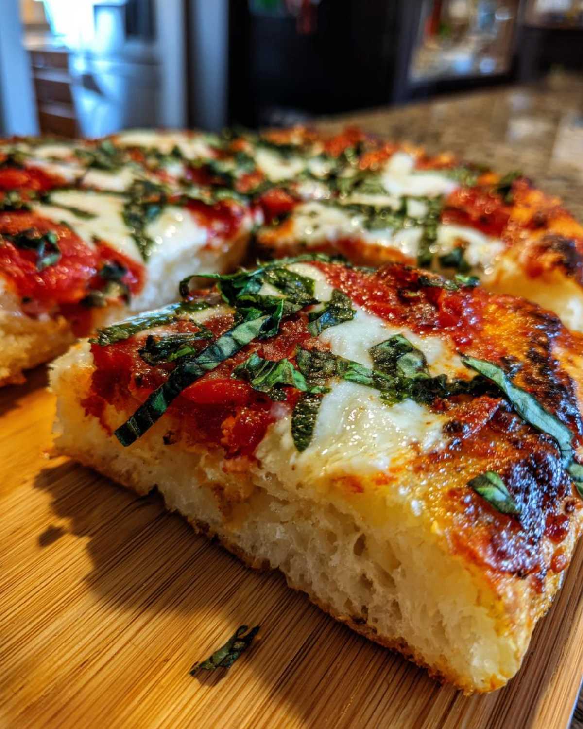 Close-up of a thick, chewy slice of Gluten-Free Margherita Pizza showing the airy crust, melted mozzarella, and fresh basil.
