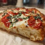 Close-up of a thick, chewy slice of Gluten-Free Margherita Pizza showing the airy crust, melted mozzarella, tomatoes, and fresh basil.