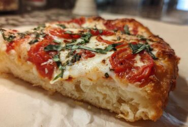 Close-up of a thick, chewy slice of Gluten-Free Margherita Pizza showing the airy crust, melted mozzarella, tomatoes, and fresh basil.