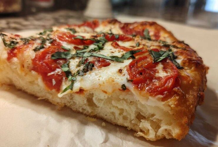 Close-up of a thick, chewy slice of Gluten-Free Margherita Pizza showing the airy crust, melted mozzarella, tomatoes, and fresh basil.