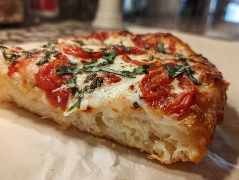 Close-up of a thick, chewy slice of Gluten-Free Margherita Pizza showing the airy crust, melted mozzarella, tomatoes, and fresh basil.