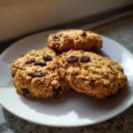 Three freshly baked Gluten-Free Oatmeal Raisin Cookies piled on a white plate, showcasing their chewy texture and visible raisins.