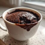 Close-up of a rich Chocolate Lava Mug Cake overflowing slightly with melted chocolate in a white mug.