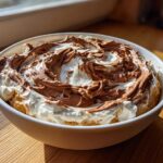 A white bowl filled with creamy Chocolate Peanut Butter Cheesecake Dip, swirled with chocolate topping.