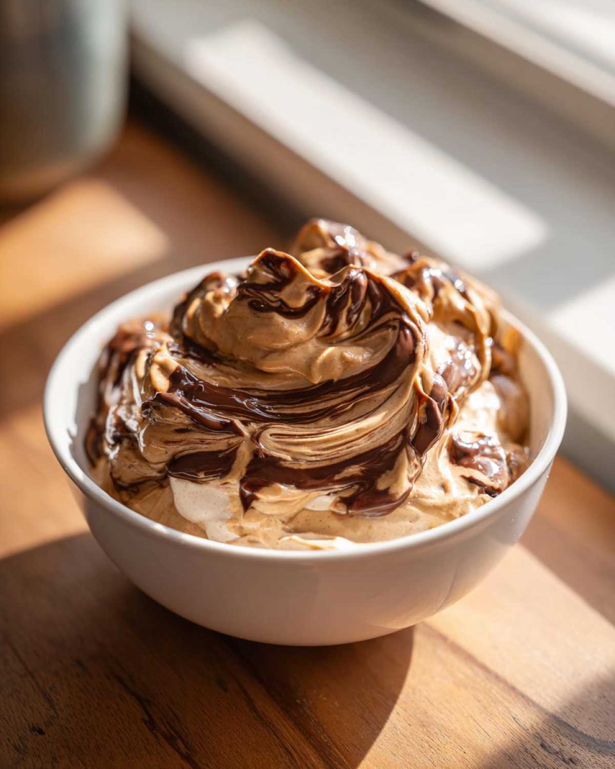 A white bowl filled with creamy Chocolate Peanut Butter Cheesecake Dip, swirled with rich chocolate sauce.