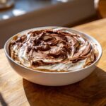A white bowl filled with Chocolate Peanut Butter Cheesecake Dip, topped with swirled chocolate and cream.