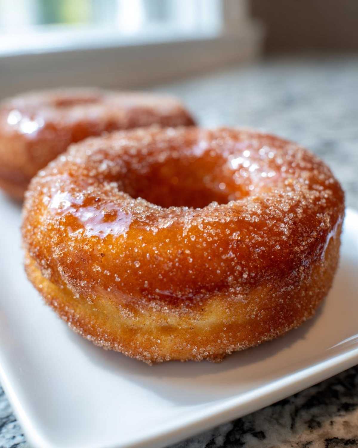 A close-up of a freshly coated Cinnamon Sugar Air Fryer Donut resting on a white plate.