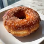 A close-up, appetizing shot of a single Cinnamon Sugar Air Fryer Donut coated in glistening sugar.