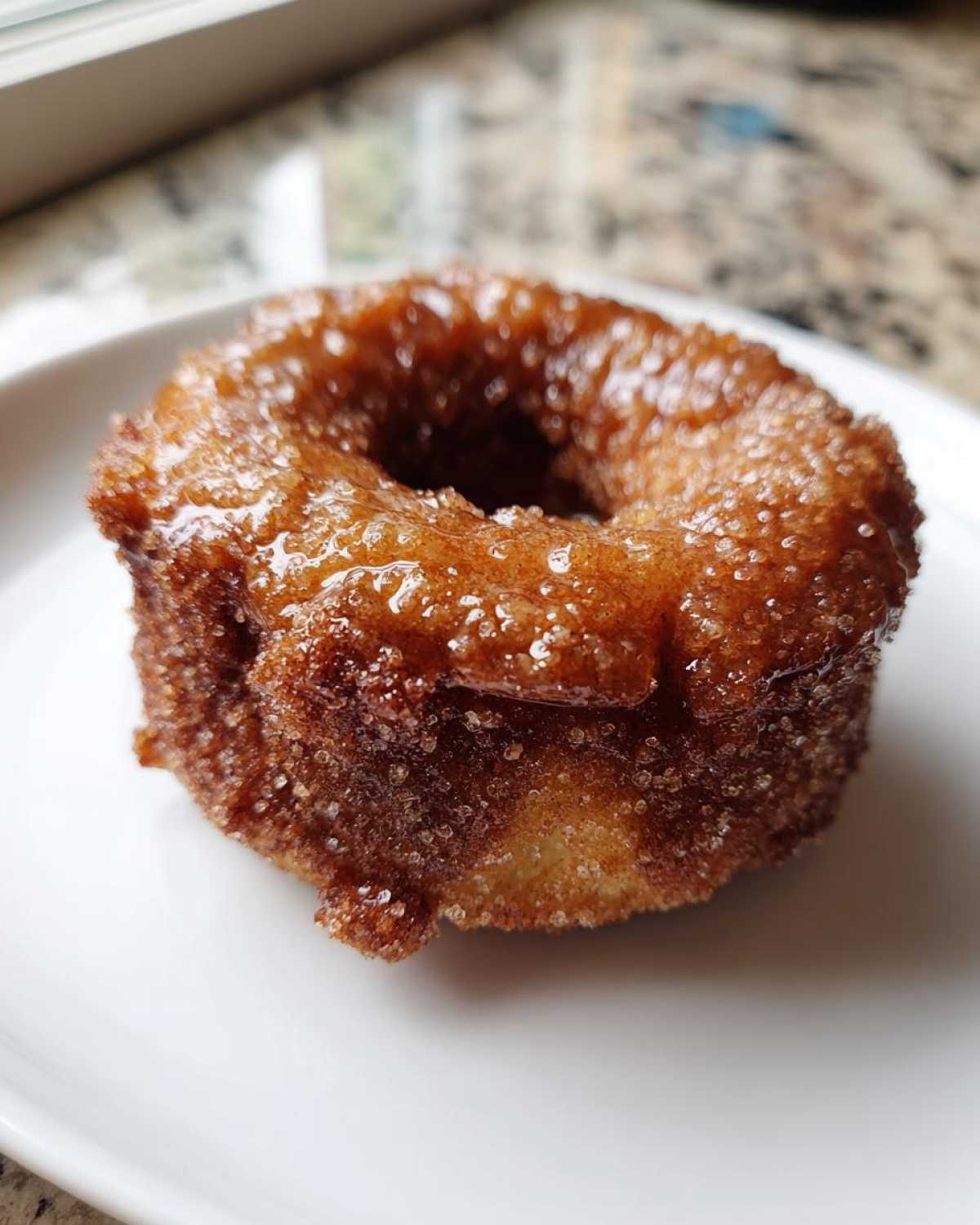 A single, glistening Cinnamon Sugar Air Fryer Donut coated in coarse sugar crystals, resting on a white plate.