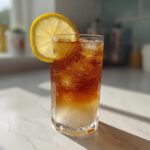 A tall glass filled with iced Cold Brew Lemonade, showing layers of liquid and condensation, garnished with a lemon slice.
