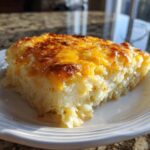 A close-up of a cheesy, baked slice of Copycat Cracker Barrel Hashbrown Casserole on a white plate.