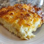 A close-up of a square serving of Copycat Cracker Barrel Hashbrown Casserole with a golden, cheesy top.