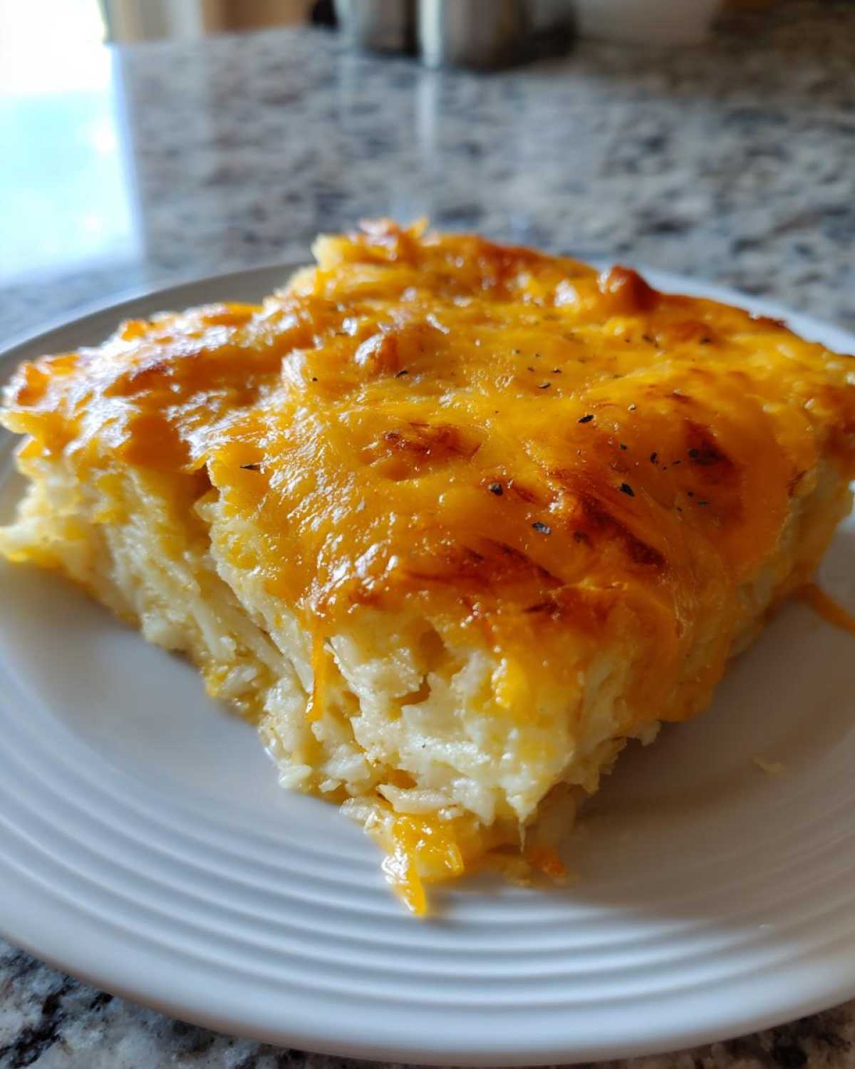 A close-up of a creamy, cheesy slice of Copycat Cracker Barrel Hashbrown Casserole on a white plate.