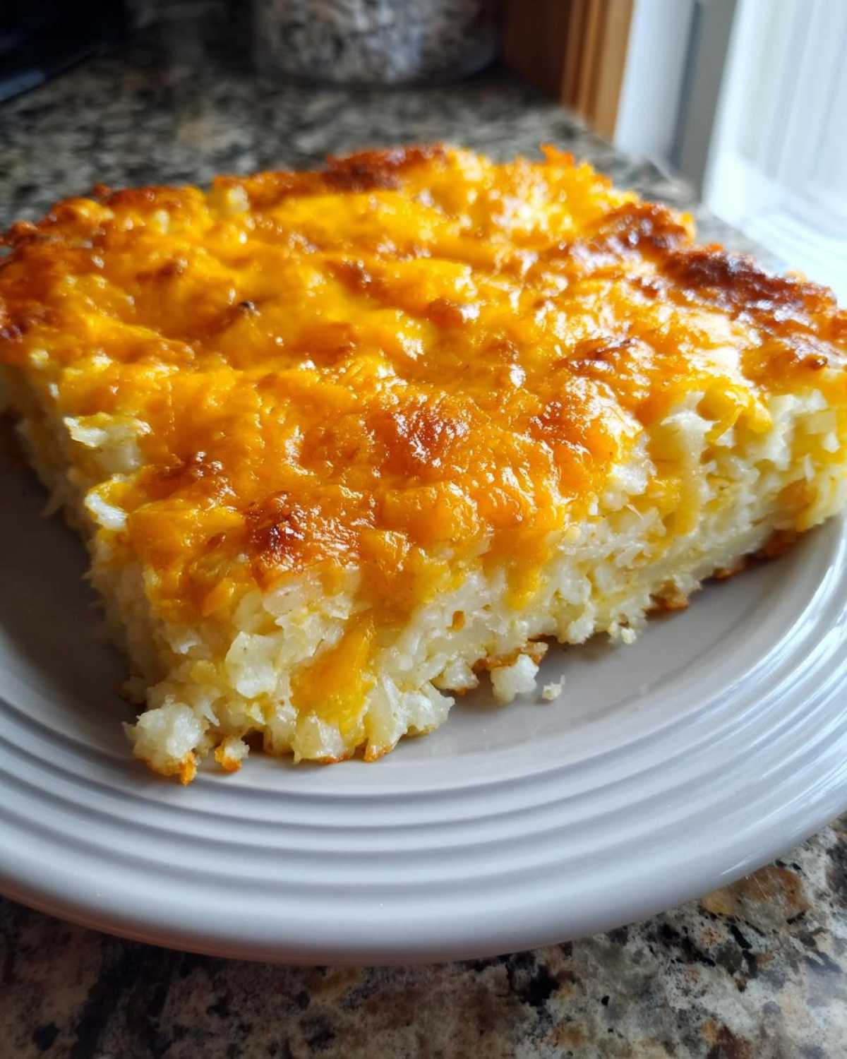 A close-up of a square slice of Copycat Cracker Barrel Hashbrown Casserole with a golden, melted cheddar cheese topping.