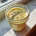 A creamy, pale yellow Copycat Olive Garden Salad Dressing topped with herbs and pepper in a glass mason jar.