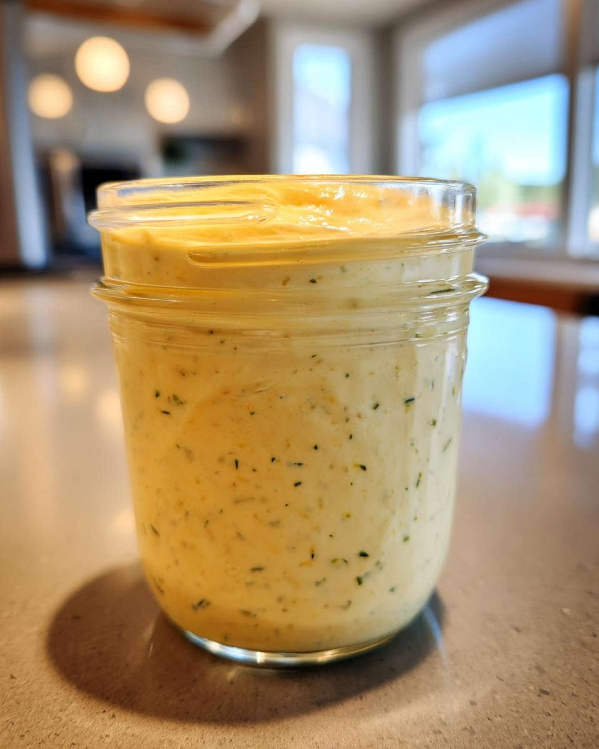A glass mason jar filled with creamy, yellow Copycat Olive Garden Salad Dressing speckled with herbs.