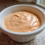 Close-up of creamy, orange-hued Copycat Raising Cane’s Sauce served in a small white ramekin.