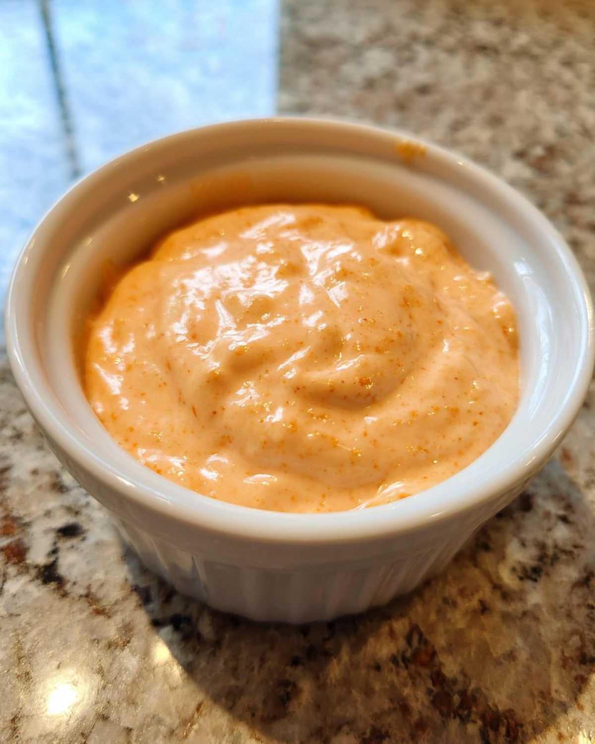 A close-up view of creamy, orange-tinted Copycat Raising Cane’s Sauce served in a small white ramekin.