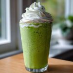 A tall glass filled with a bright green Copycat Shamrock Shake topped with whipped cream.
