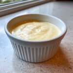 A small white ramekin filled with creamy, yellowish Copycat Taco Bell Chicken Quesadilla Sauce.