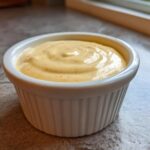 A close-up of creamy, orange-flecked Copycat Taco Bell Chicken Quesadilla Sauce in a white ramekin.