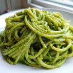 A mound of spaghetti coated in bright green, creamy avocado pasta sauce, served on a white plate.