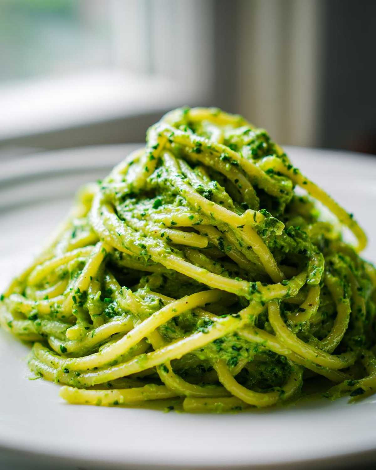A close-up shot of spaghetti tossed in vibrant green Creamy Avocado Pasta sauce, served on a white plate.