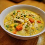 Close-up of creamy Chicken Pot Pie Soup featuring shredded chicken, bright orange carrots, green peas, and corn kernels.