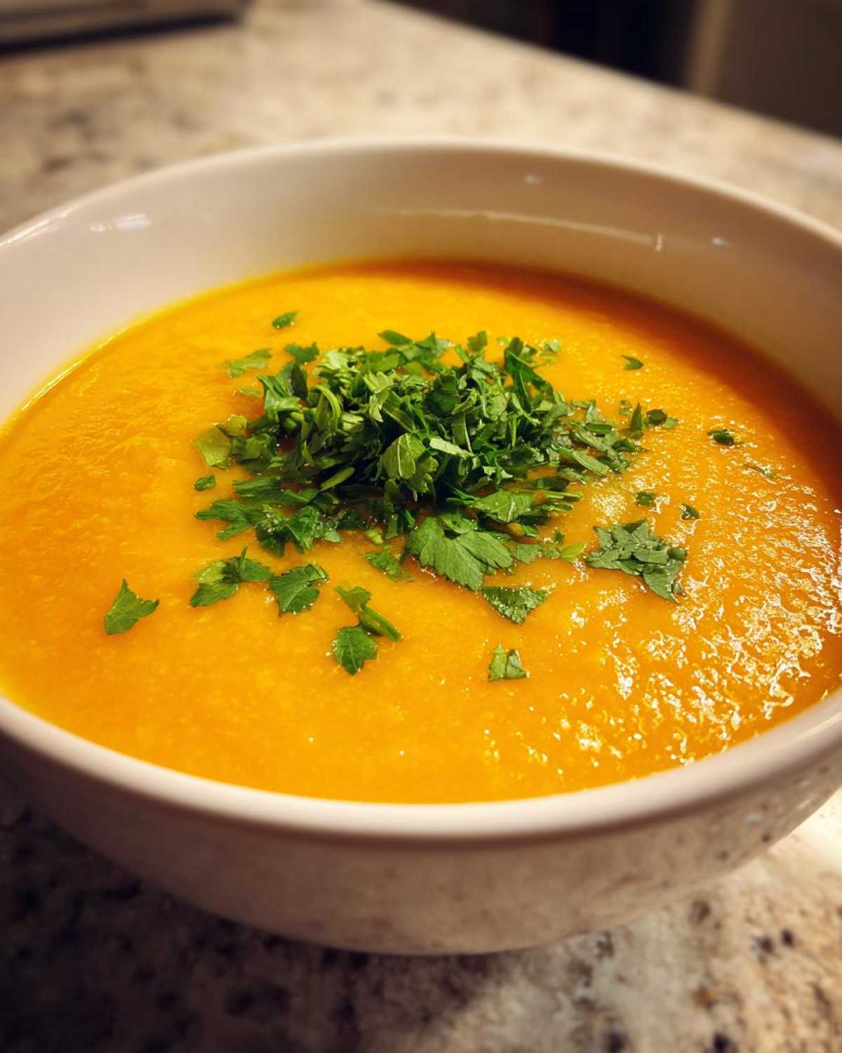 Close-up of a vibrant orange bowl of Creamy Coconut Lentil Soup topped with fresh chopped cilantro or parsley.