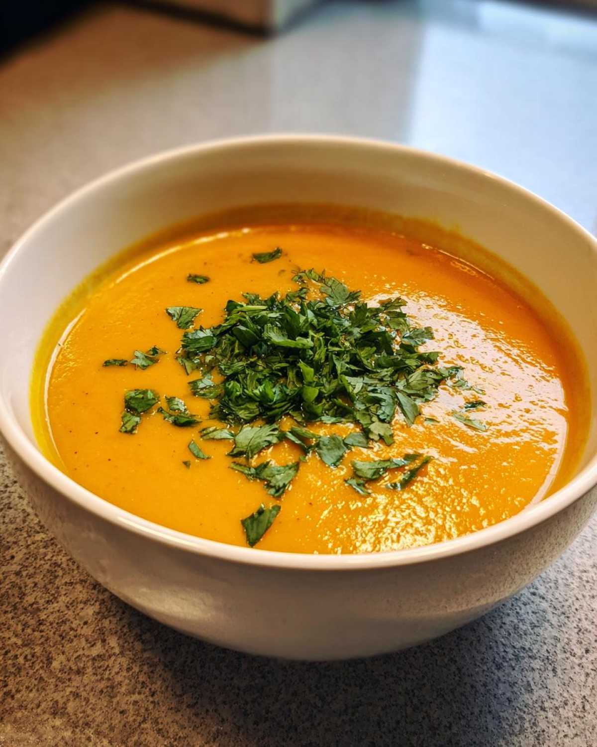 Close-up of a bowl of bright orange Creamy Coconut Lentil Soup topped with fresh chopped parsley.