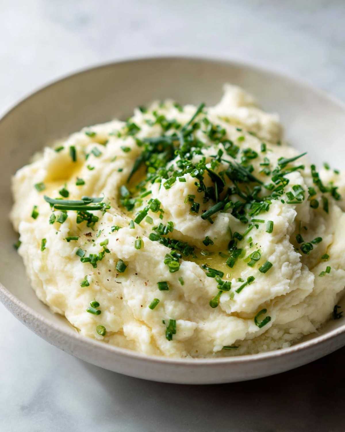 A close-up of fluffy Creamy Garlic Mashed Cauliflower topped with melted butter and fresh chopped chives.