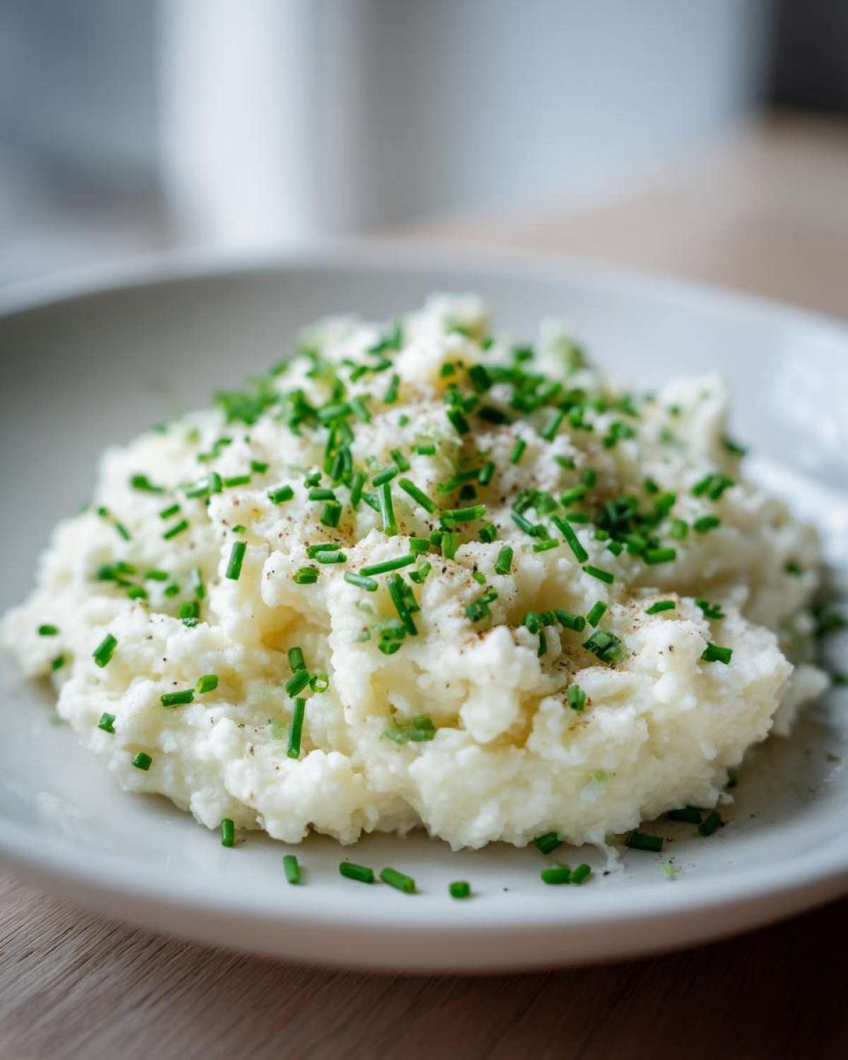 A mound of Creamy Garlic Mashed Cauliflower topped generously with fresh chopped chives and pepper.