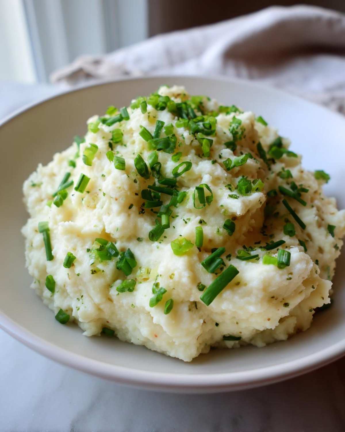A bowl of fluffy Creamy Garlic Mashed Cauliflower topped generously with fresh, chopped green chives.