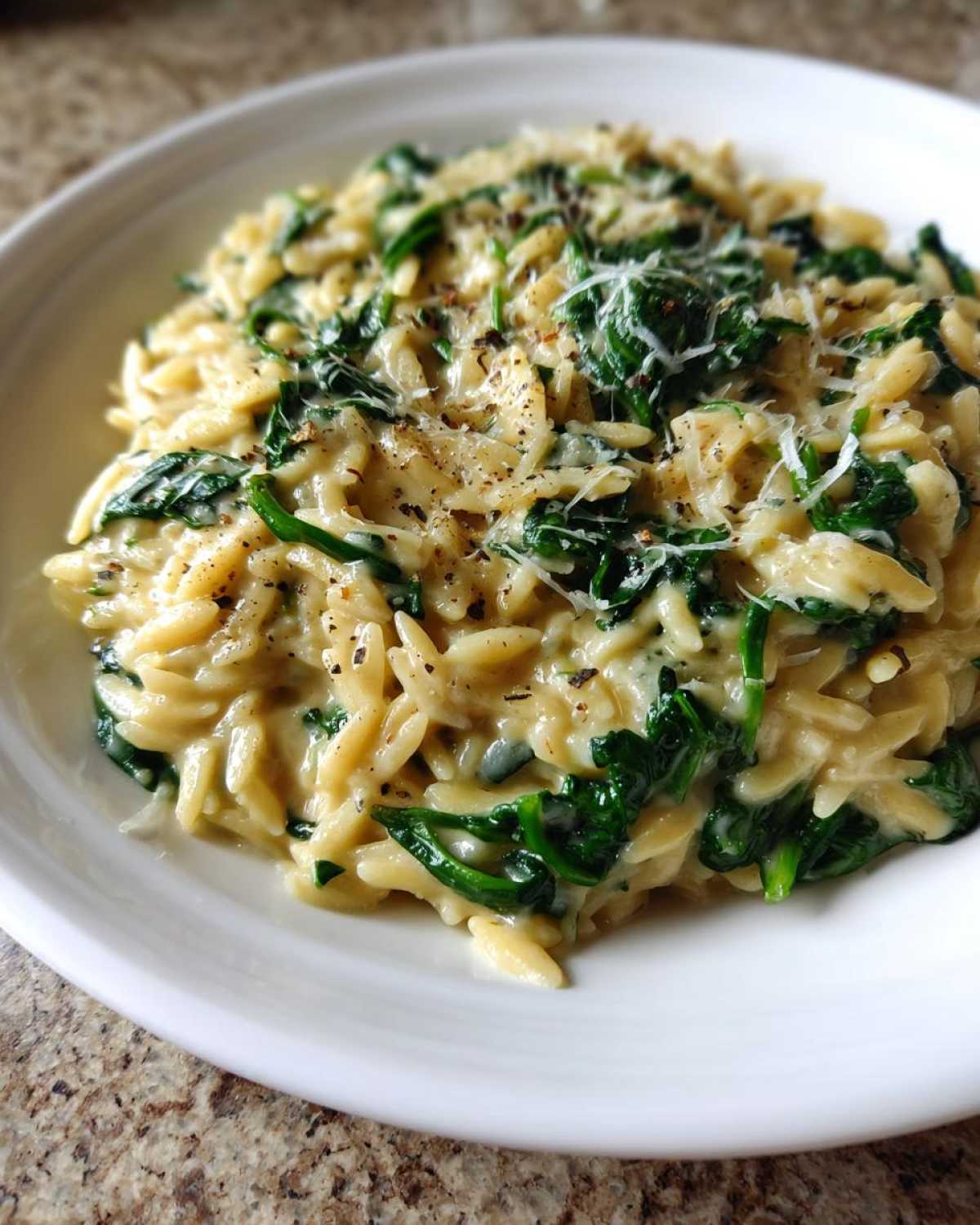 A close-up of creamy garlic parmesan orzo with spinach, topped with grated cheese and black pepper.