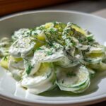 Close-up of sliced cucumbers generously coated in a creamy dressing and topped with fresh dill, representing Creamy German Cucumber Salad.
