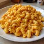 A close-up of a generous serving of creamy, bright orange Instant Pot Mac and Cheese on a white plate.