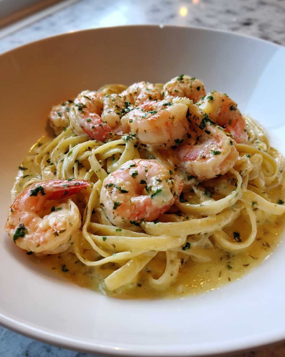 A close-up of a white bowl filled with Creamy Lemon Garlic Shrimp Pasta, topped with large shrimp and fresh parsley.