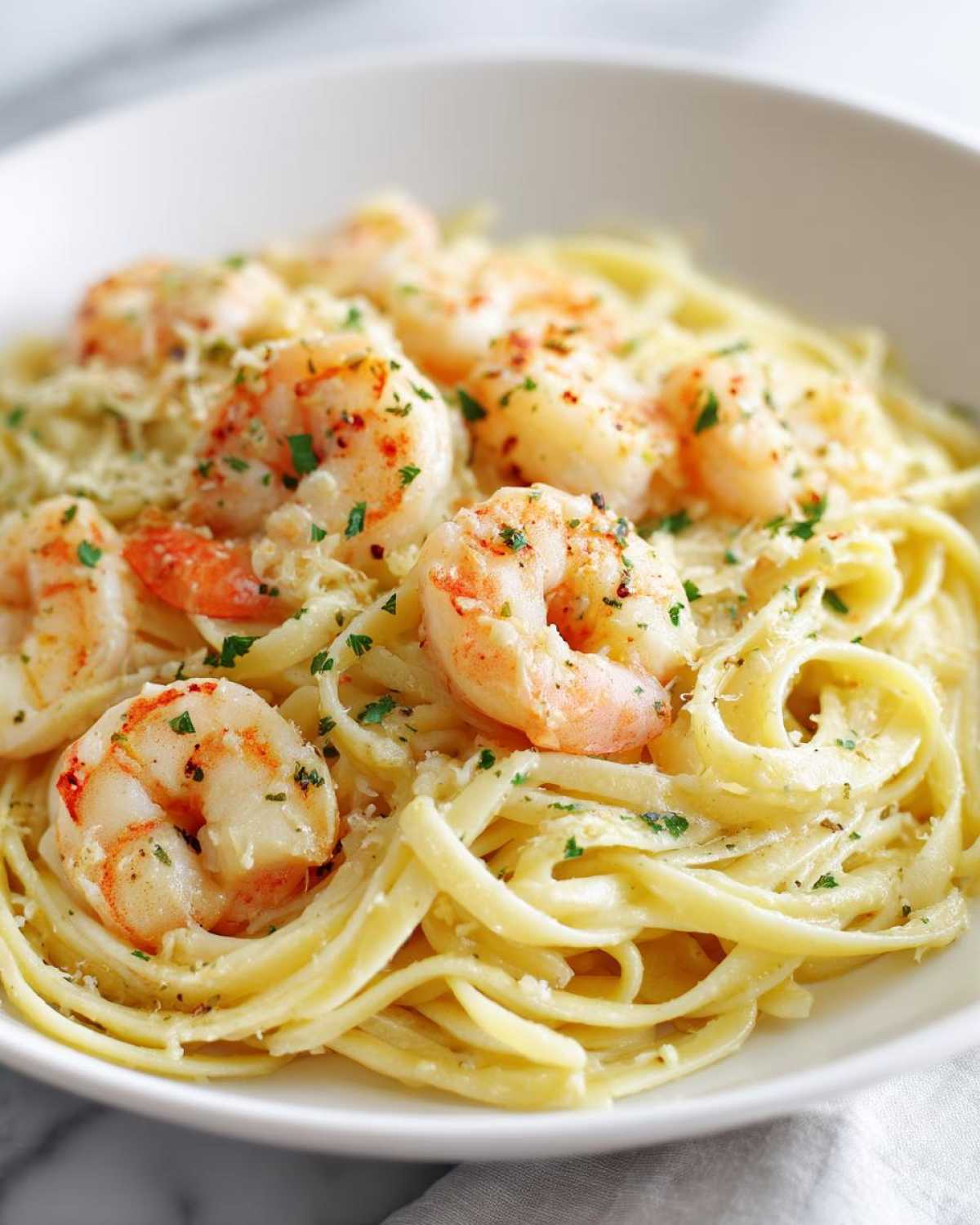 A close-up of fettuccine pasta coated in a creamy sauce, topped with seasoned shrimp and parsley, showcasing the Creamy Lemon Garlic Shrimp Pasta.
