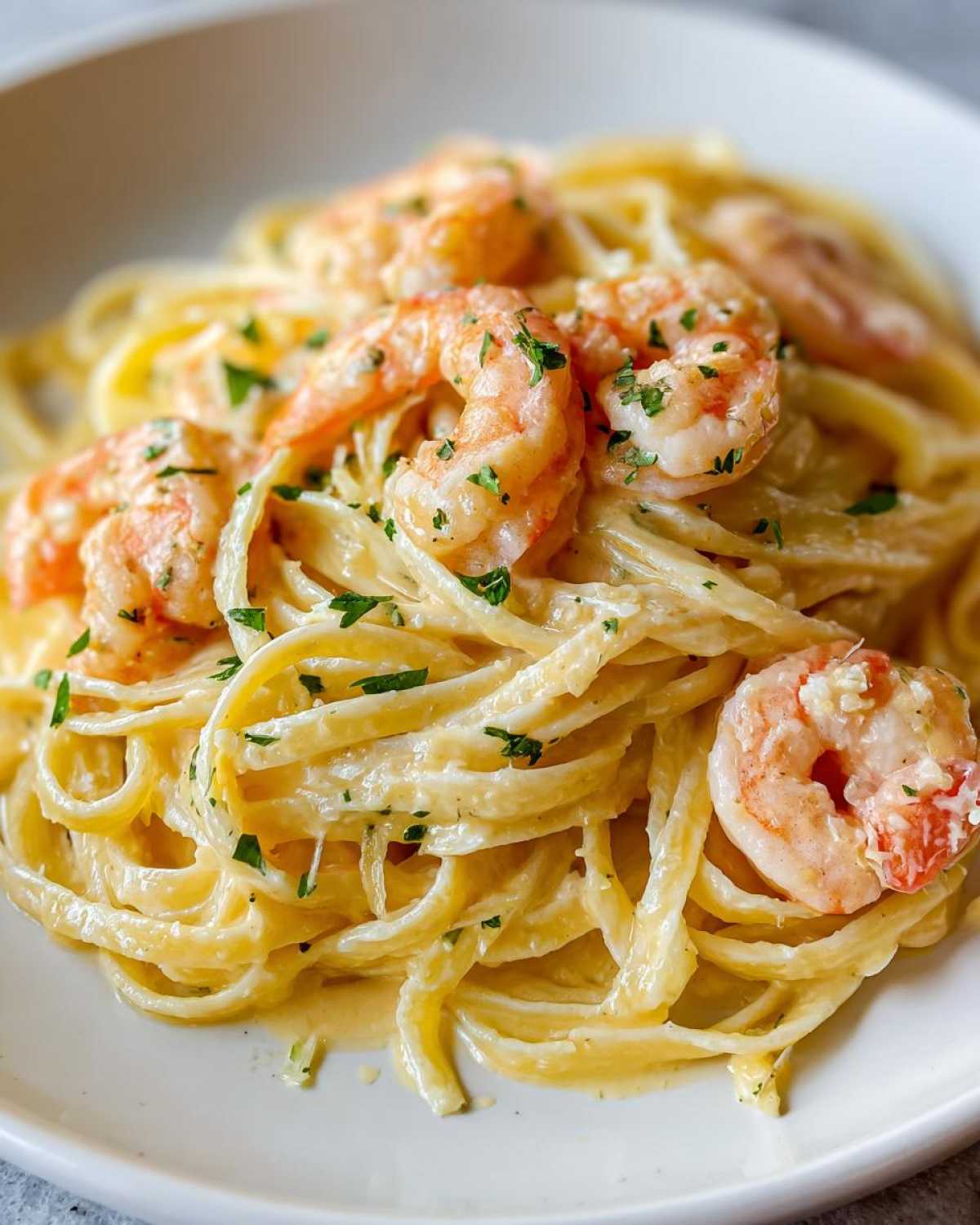 Close-up of linguine coated in a rich sauce, topped with pink shrimp and fresh parsley for Creamy Lemon Garlic Shrimp Pasta.