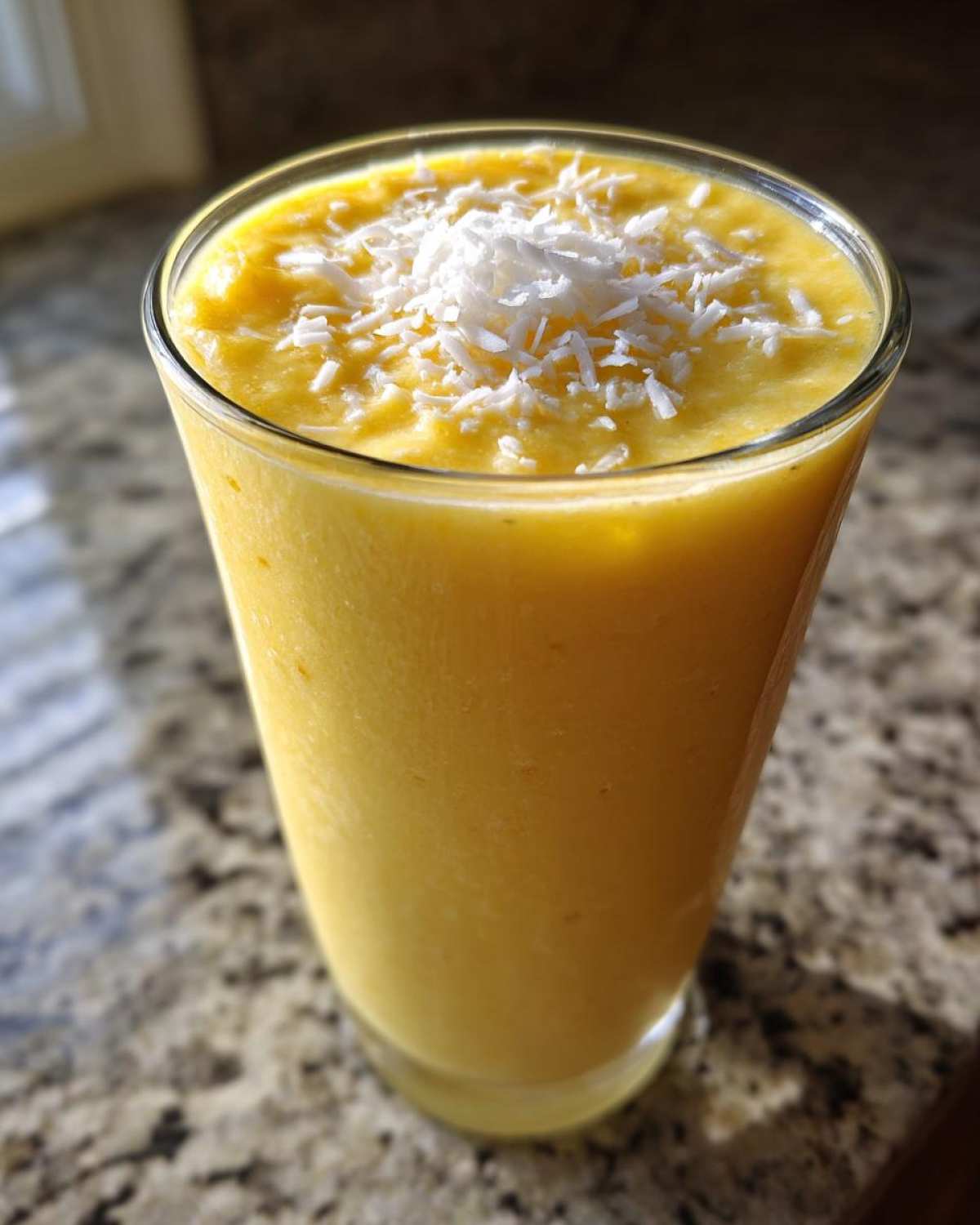 A tall glass filled with a vibrant yellow Pineapple Coconut Smoothie, topped with shredded coconut.