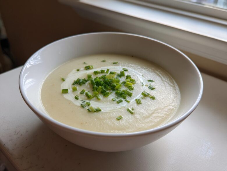 A white bowl filled with smooth, creamy potato leek soup, garnished with a swirl of cream and fresh chopped chives.