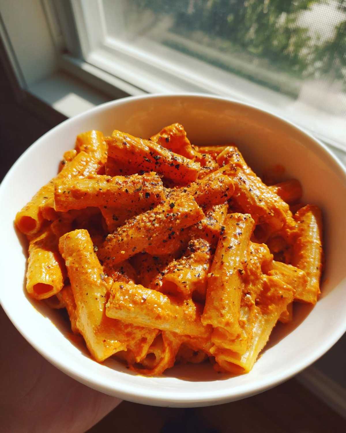 Close-up of rigatoni pasta coated in bright orange Creamy Roasted Red Pepper Pasta sauce, topped with cracked black pepper.