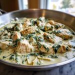 Close-up of seared chicken pieces swimming in a rich, creamy sauce with spinach and artichoke hearts: Creamy Spinach Artichoke Chicken Skillet.