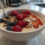 A close-up of a Creamy Vanilla Protein Smoothie Bowl topped with fresh raspberries, blueberries, sliced strawberries, and almonds.